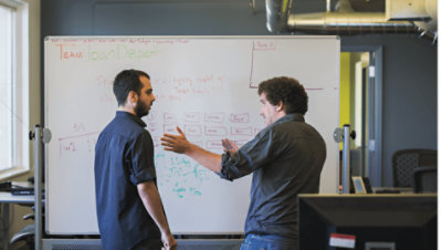 ホワイトボードの前で会話をしている 2 人の人