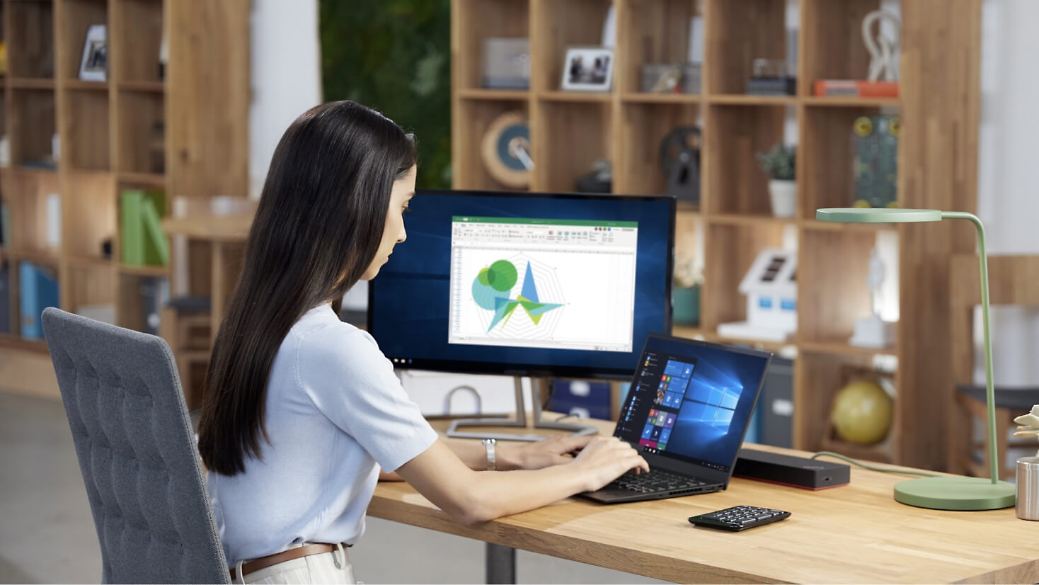 En person, der arbejder ved sit skrivebord med en bærbar computer og en stationær skærm.