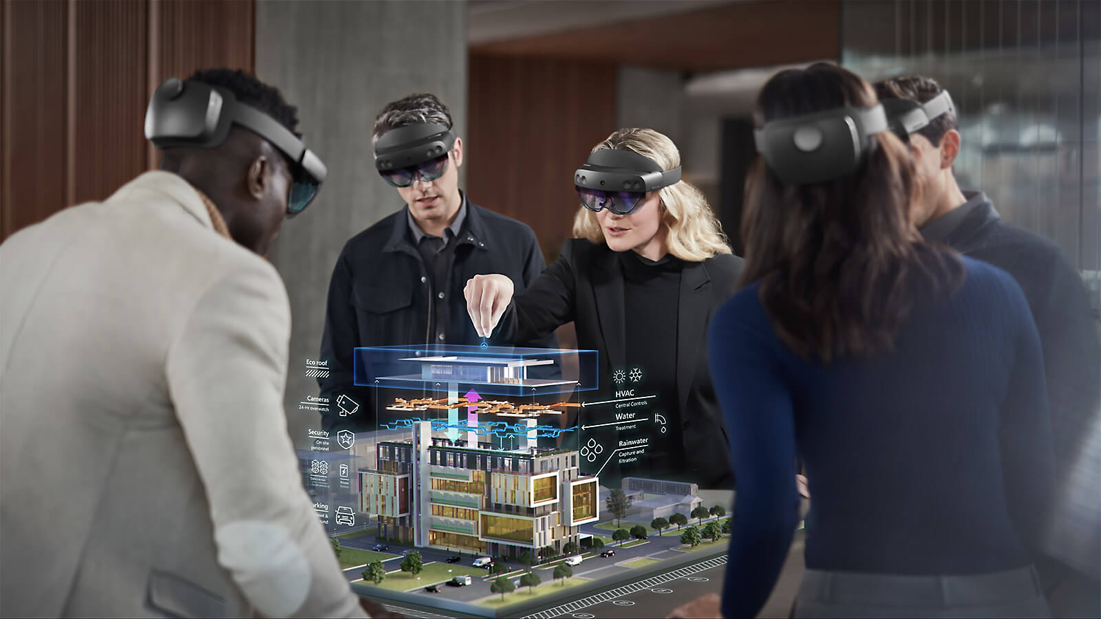 Masanın etrafında ayakta durup taktıkları HoloLens 2 cihazlarıyla karma gerçeklikte mimari tasarımları görüntüleyen beş kişi