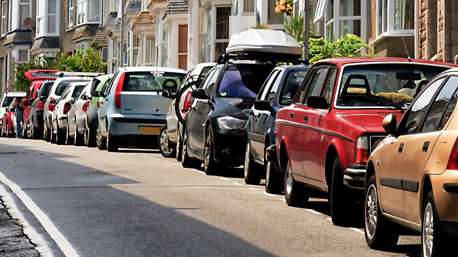 Vehicles parked along a suburban street with their side mirrors extended.