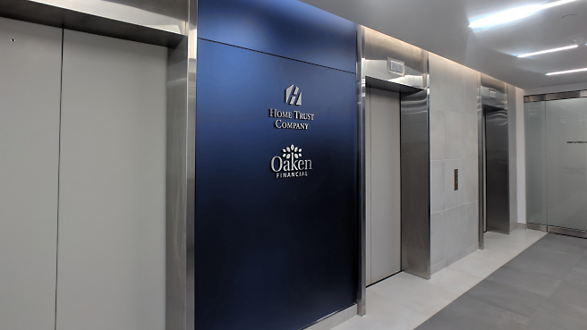 現代化的辦公室大廳，電梯旁的金屬牆上有 Home Trust Company 和 Oaken Financial 的招牌。