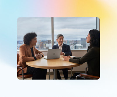 Tre personer sitter ved et rundt bord i et kontormiljø som er engasjert i en diskusjon.