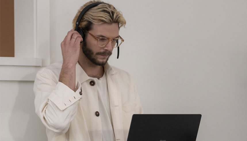 A male adjusts his Microsoft Modern USB headset, while looking at his Surface laptop