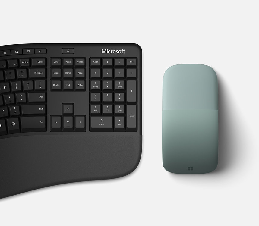 Microsoft Arc Mouse sits next to a keyboard.
