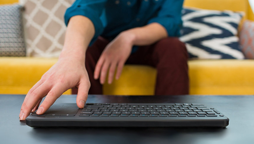 A person uses a wireless Microsoft keyboard while sitting on a couch.