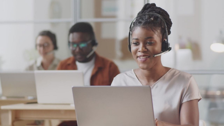 Een vrouw die een headset draagt terwijl ze op een laptop werkt.
