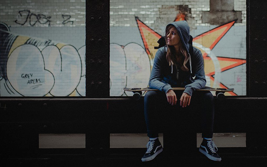 Eine junge Frau mit Kapuzenshirt sitzt einem Graffiti besprühten Tunnel und schaut zur Seite