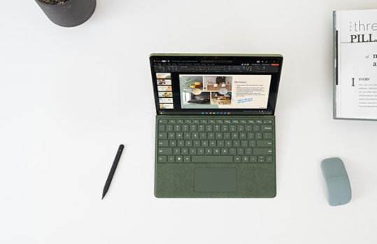 Surface Pro 9 を机の上に開いて PowerPoint を表示し、スリム ペンとマウスを使用している画像
