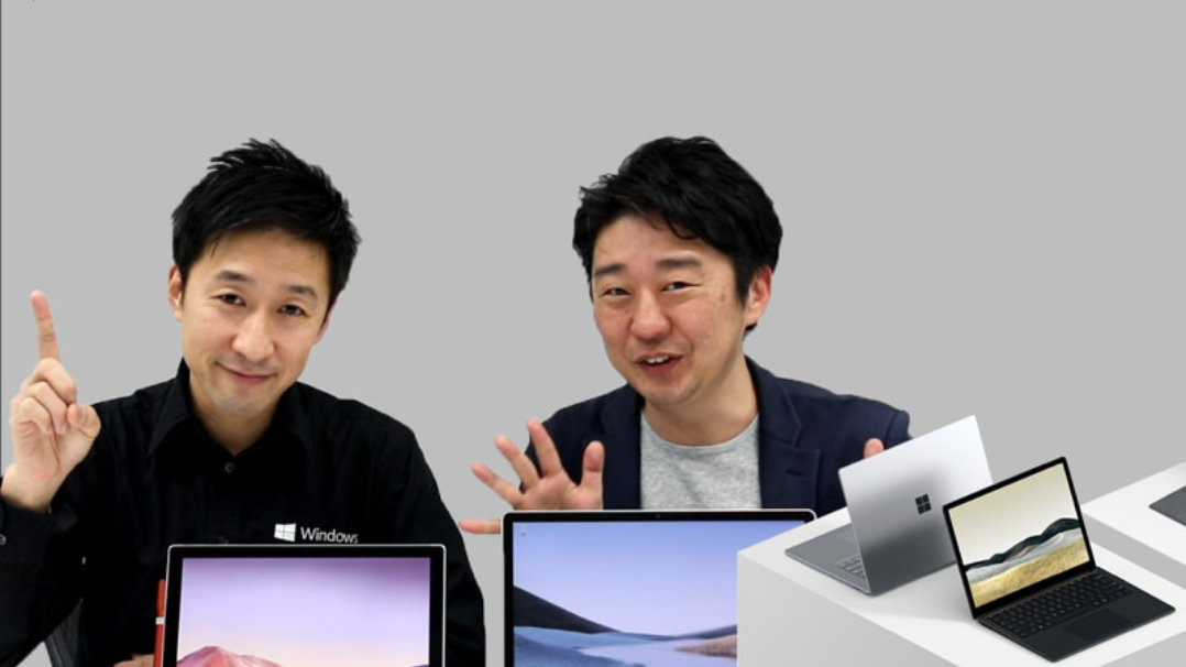 複数の Surface デバイスの前で手を上げる 2 人の男性