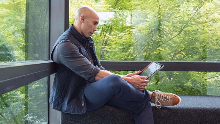 Man sitting against office building window working on a laptop.