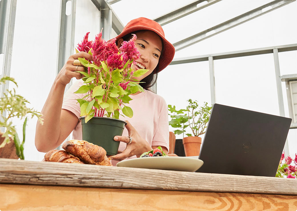 ノート PC を見ながら植物の世話をする女性