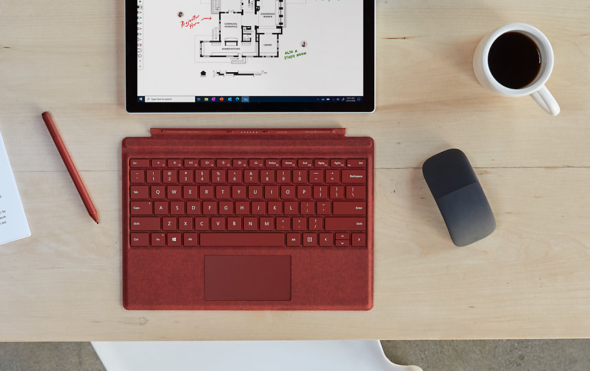Eine Microsoft Arc Mouse befindet sich auf einem Schreibtisch neben einem Surface-Gerät.