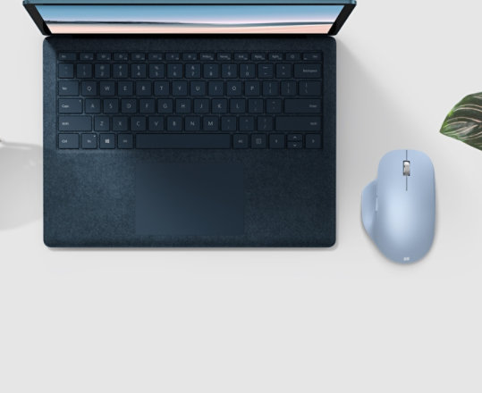 Microsoft Bluetooth Ergonomic Mouse next to a laptop, plant, and fan.