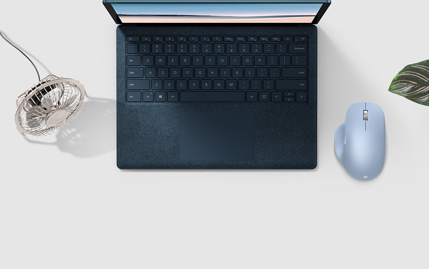 Microsoft Bluetooth Ergonomic Mouse next to a laptop, plant and fan.