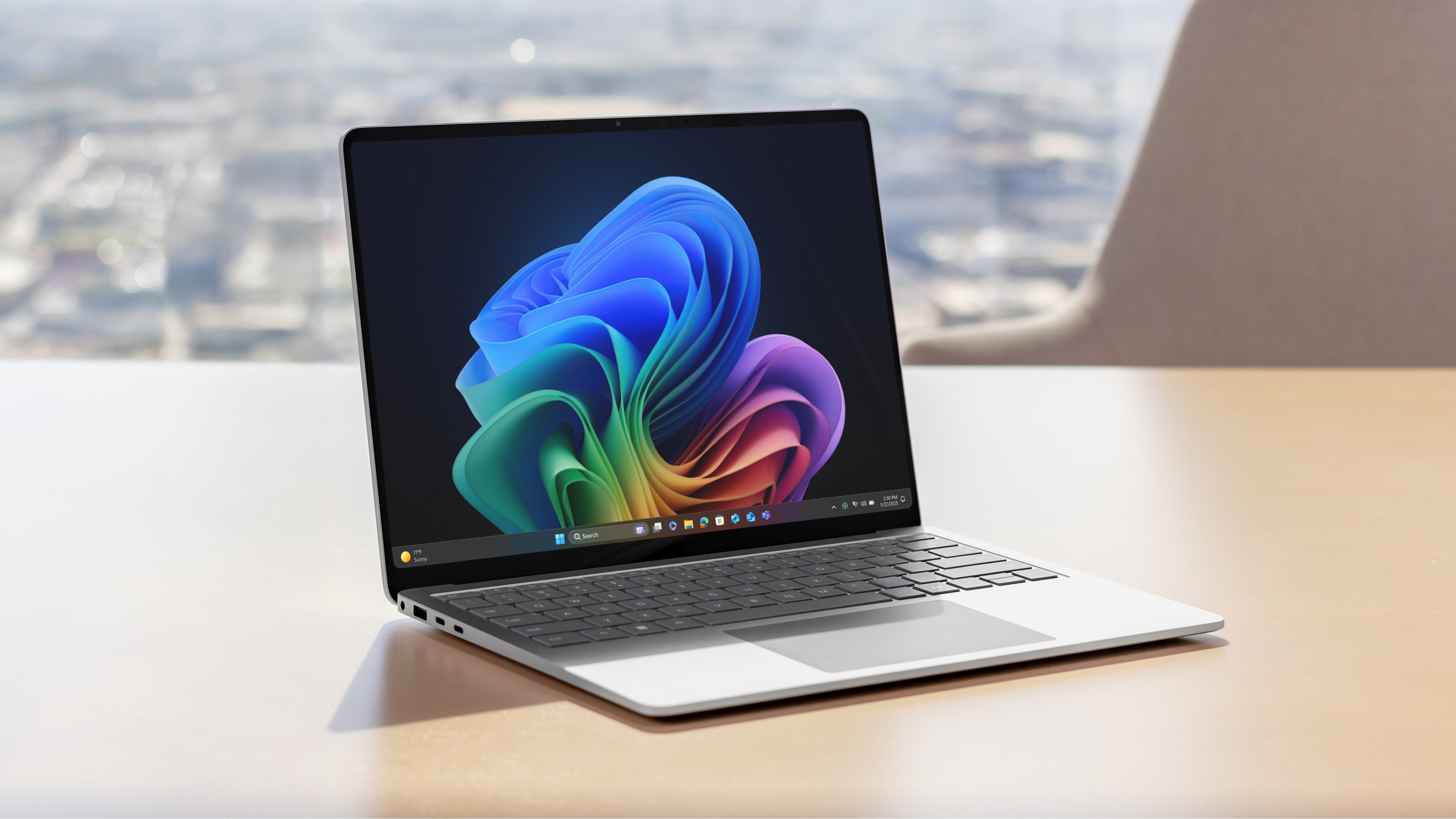 Un ordinateur portable Surface Laptop ouvert avec un écran PixelSense™ vif et antireflet qui affiche une image de fleur arc-en-ciel sur un bureau beige avec une chaise et un paysage urbain en arrière-plan.