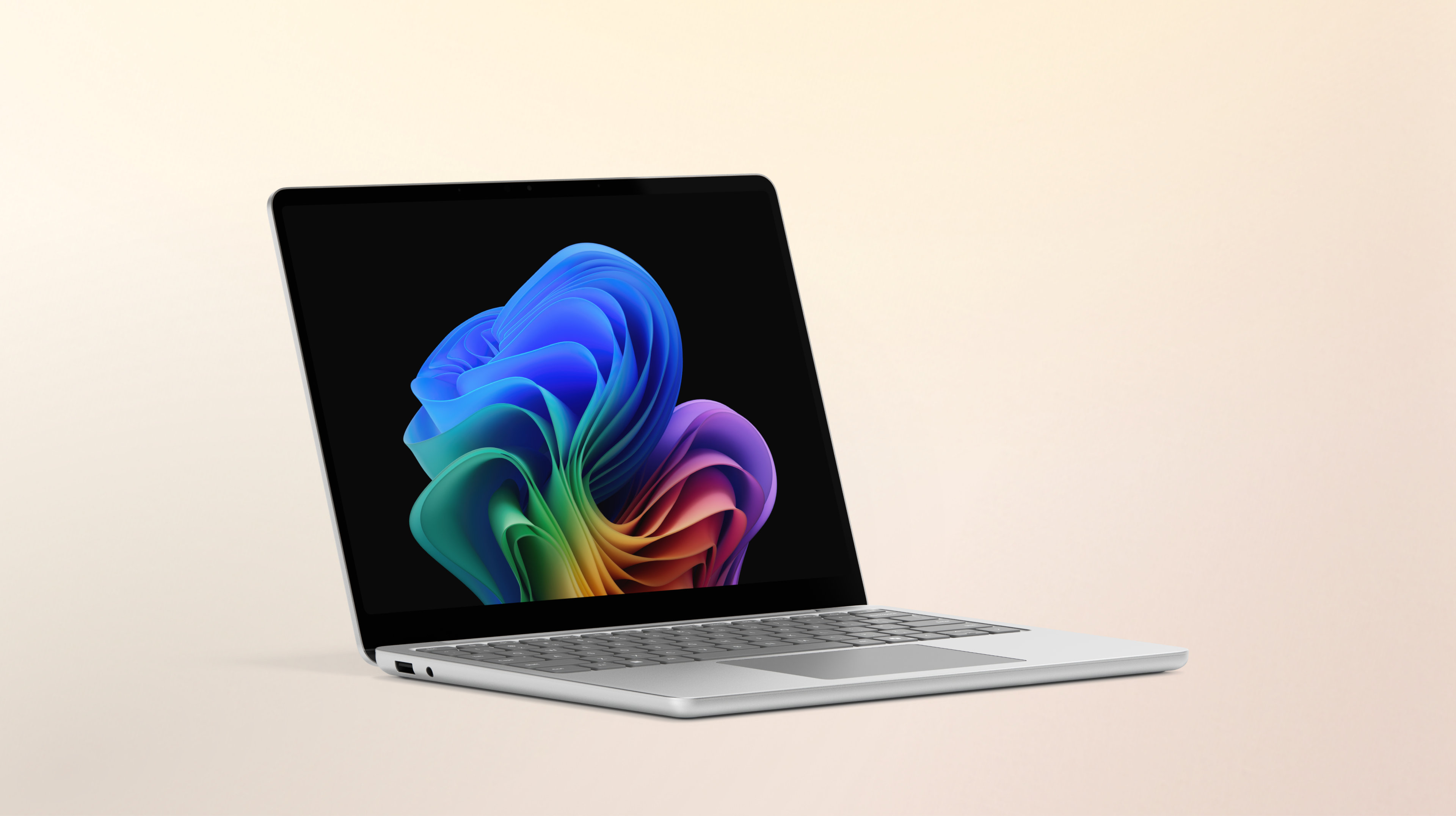 An open built-in AI platinum Surface Laptop facing right displaying the rainbow bloom image against a gradient peach background
