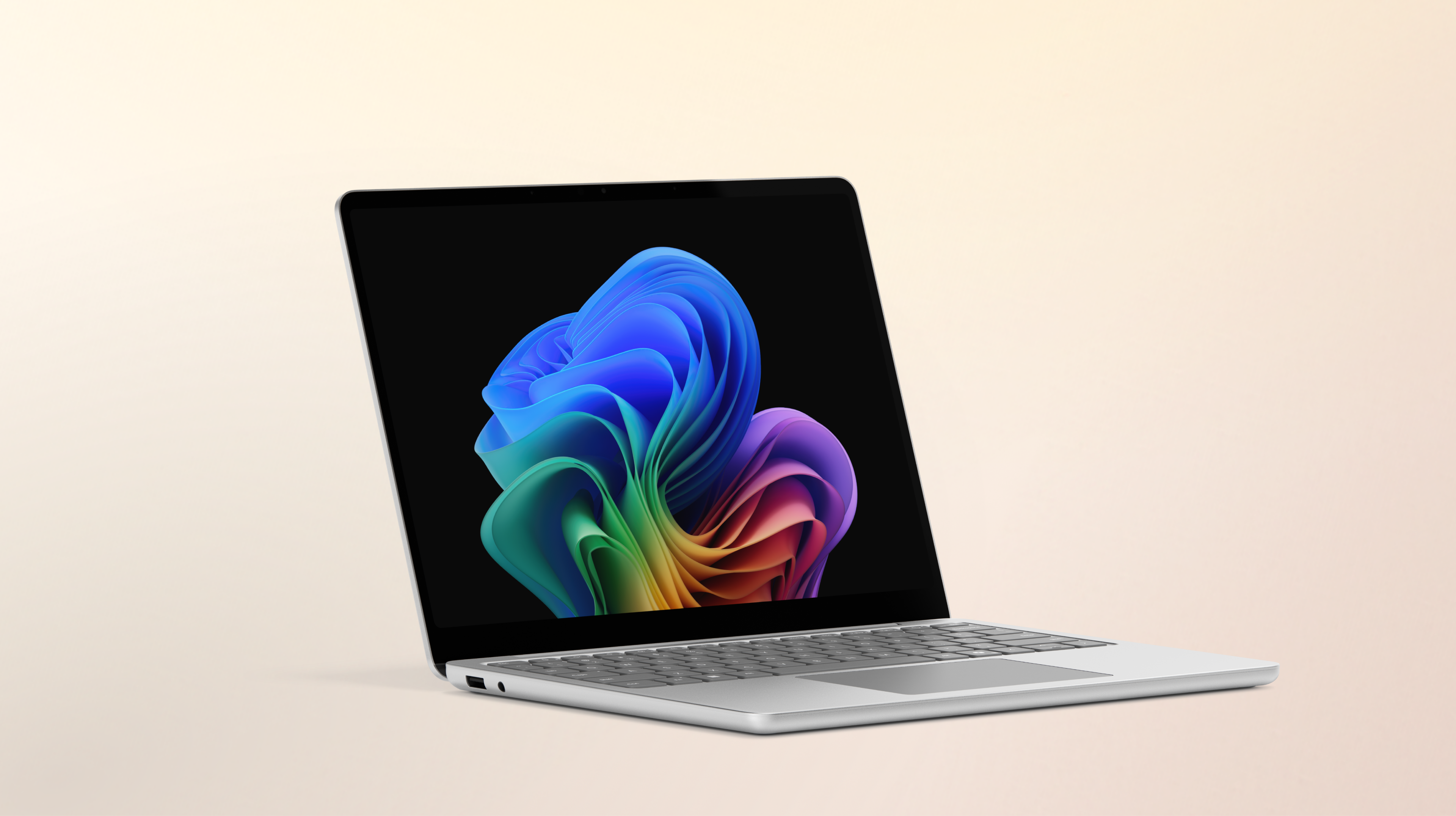 Un ordinateur portable Surface Laptop Copilot+ platine ouvert, tourné vers la droite, affichant l'image de la fleur arc-en-ciel sur un arrière-plan pêche dégradé.