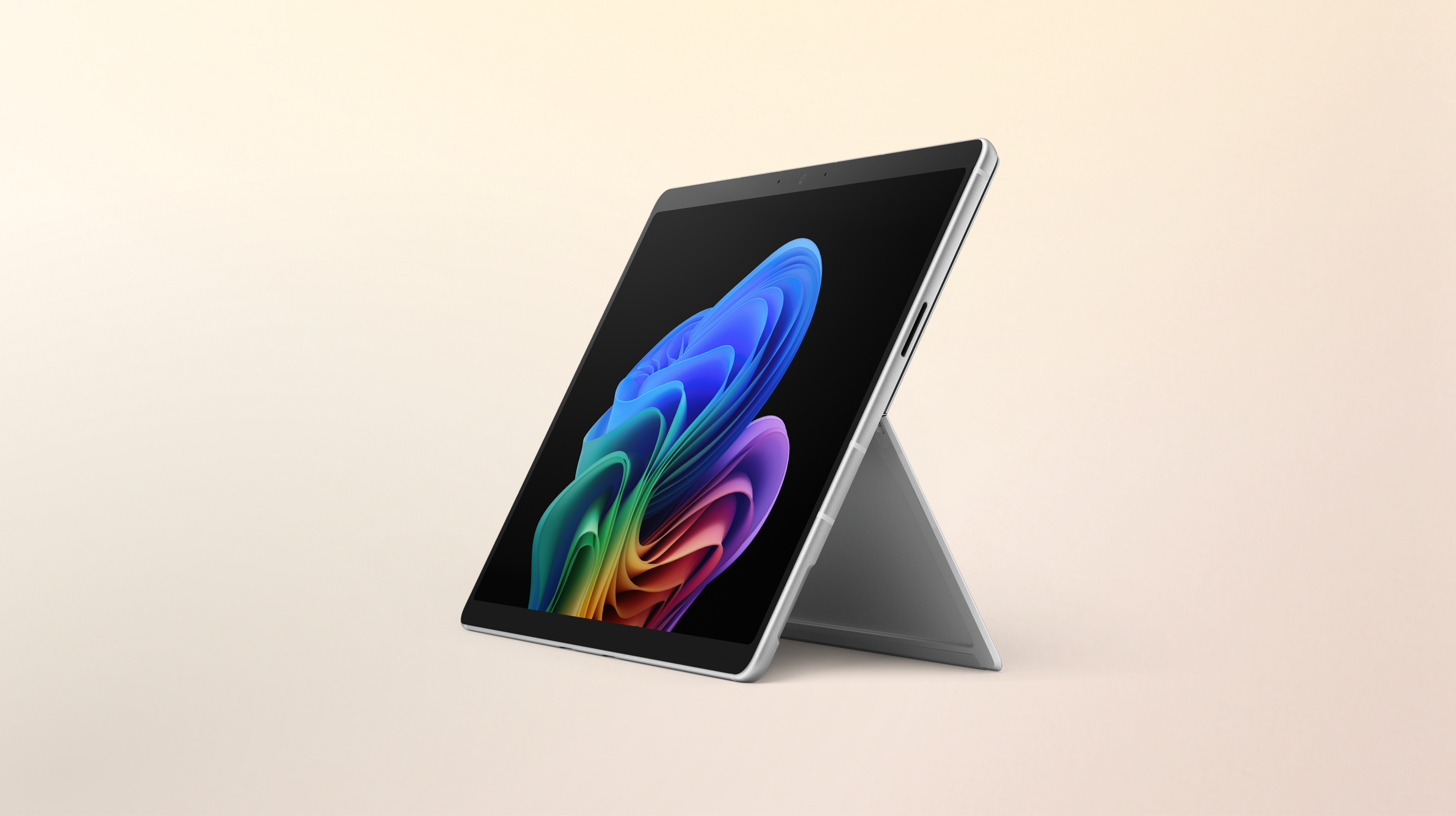 An open Surface Pro 2-in-1 facing left without a keyboard displaying the rainbow bloom image against a gradient peach background