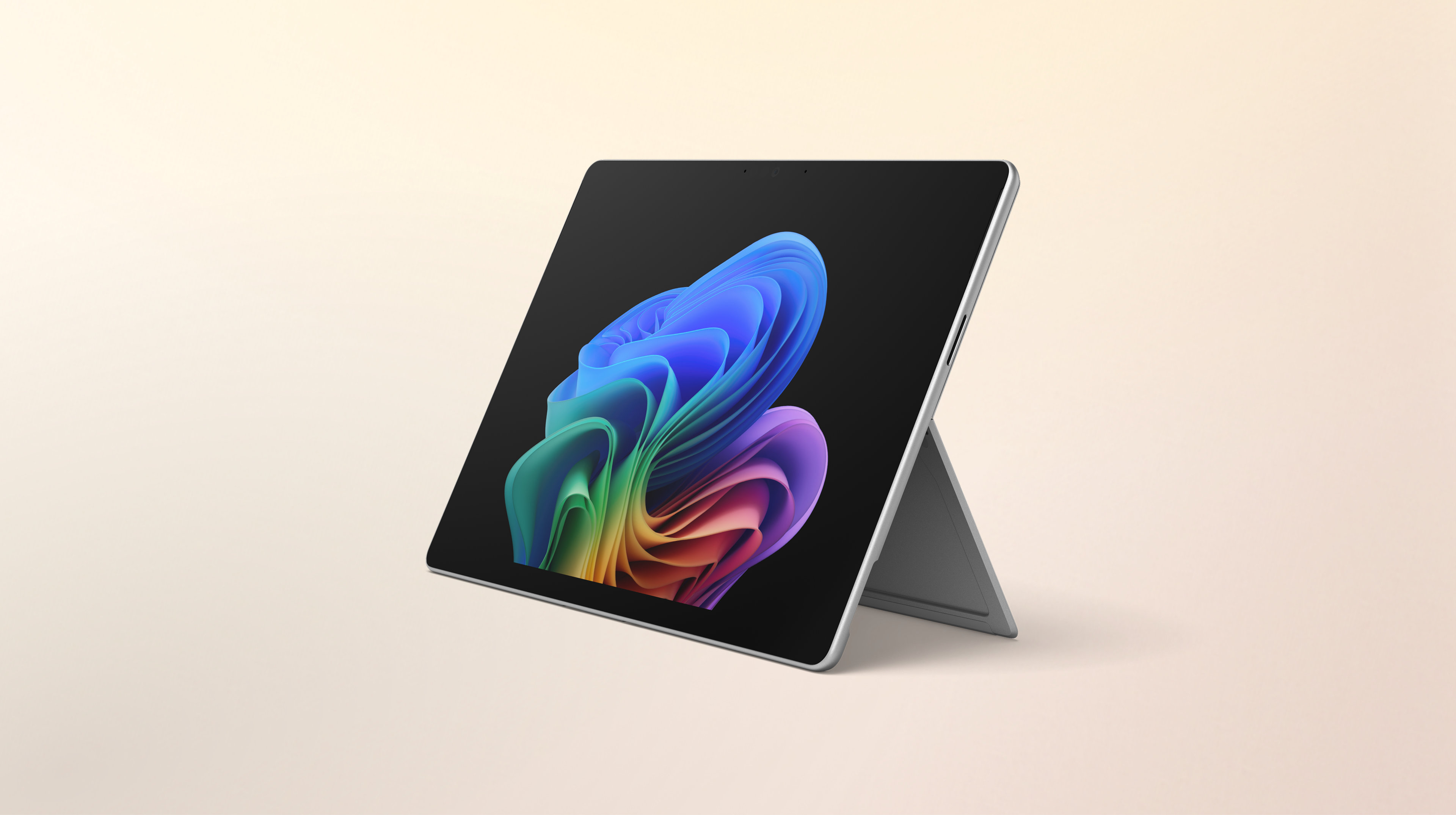 Un ordinateur portable Windows Surface Pro ouvert, tourné vers la gauche, sans clavier, affichant l'image de la fleur arc-en-ciel sur un arrière-plan pêche dégradé.
