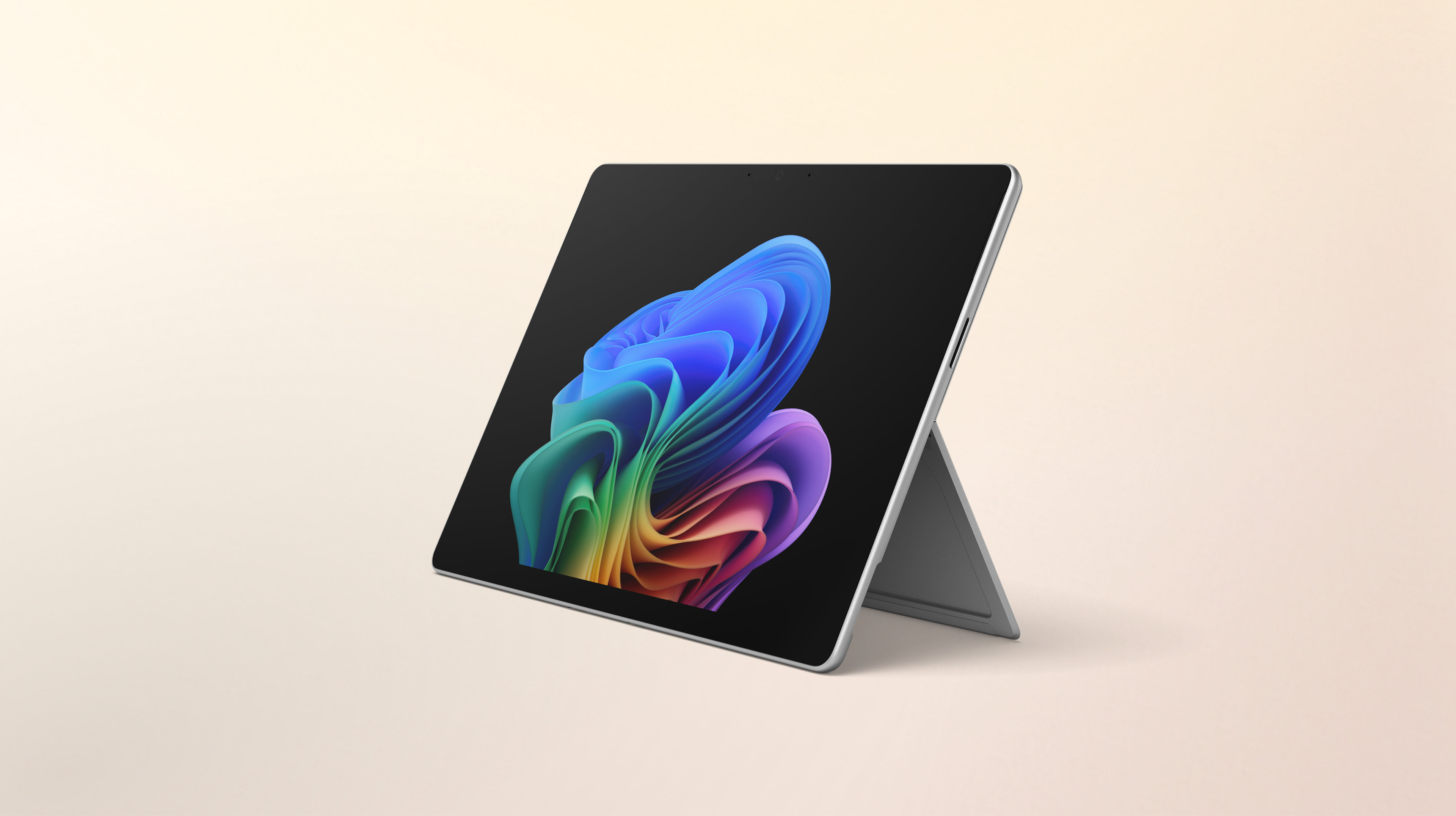 Un ordinateur portable Windows Surface Pro ouvert, tourné vers la gauche, sans clavier, affichant l'image de la fleur arc-en-ciel sur un arrière-plan pêche dégradé.