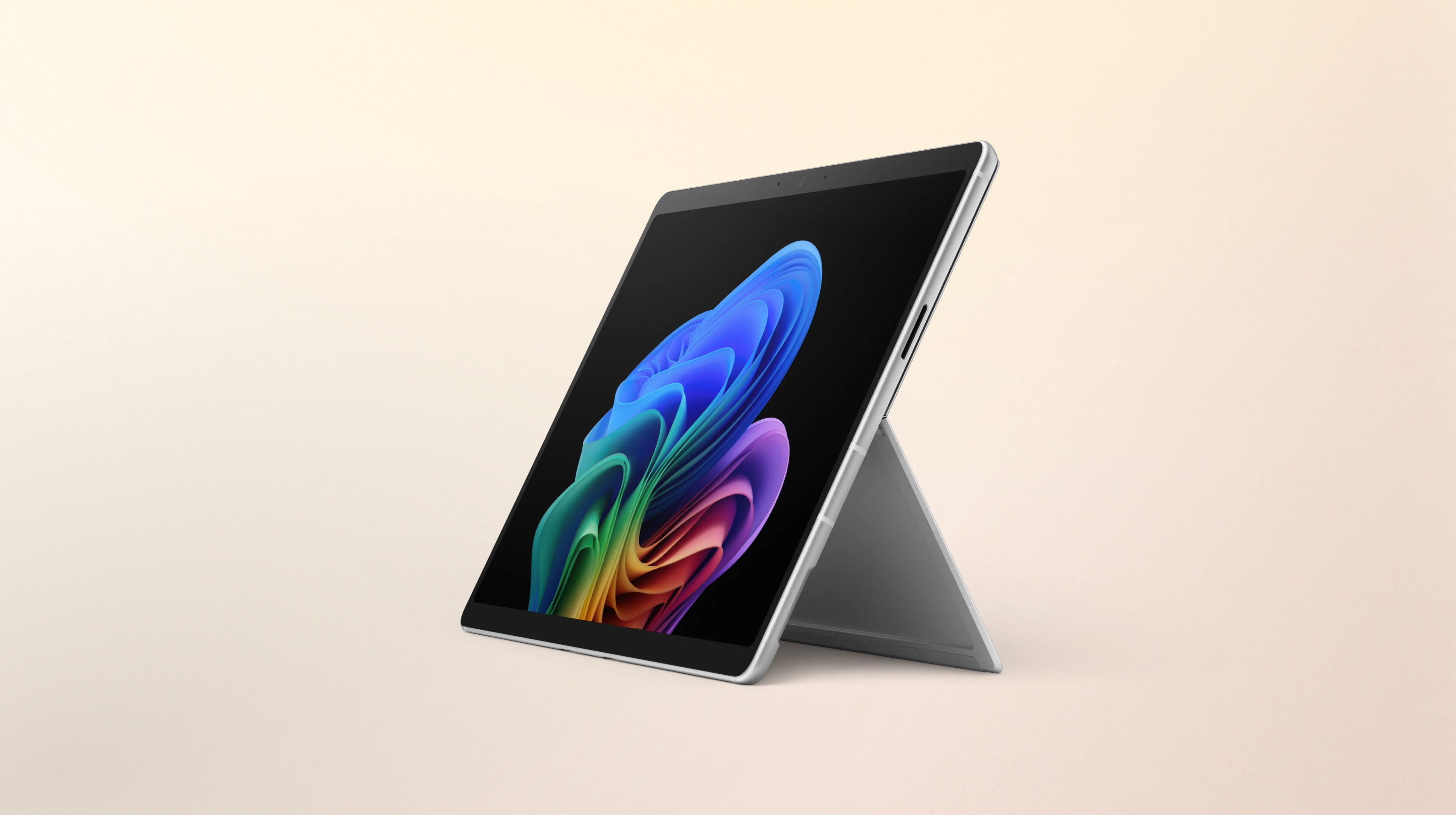 Un ordinateur portable Windows Surface Pro ouvert, tourné vers la gauche, sans clavier, affichant l'image de la fleur arc-en-ciel sur un arrière-plan pêche dégradé.