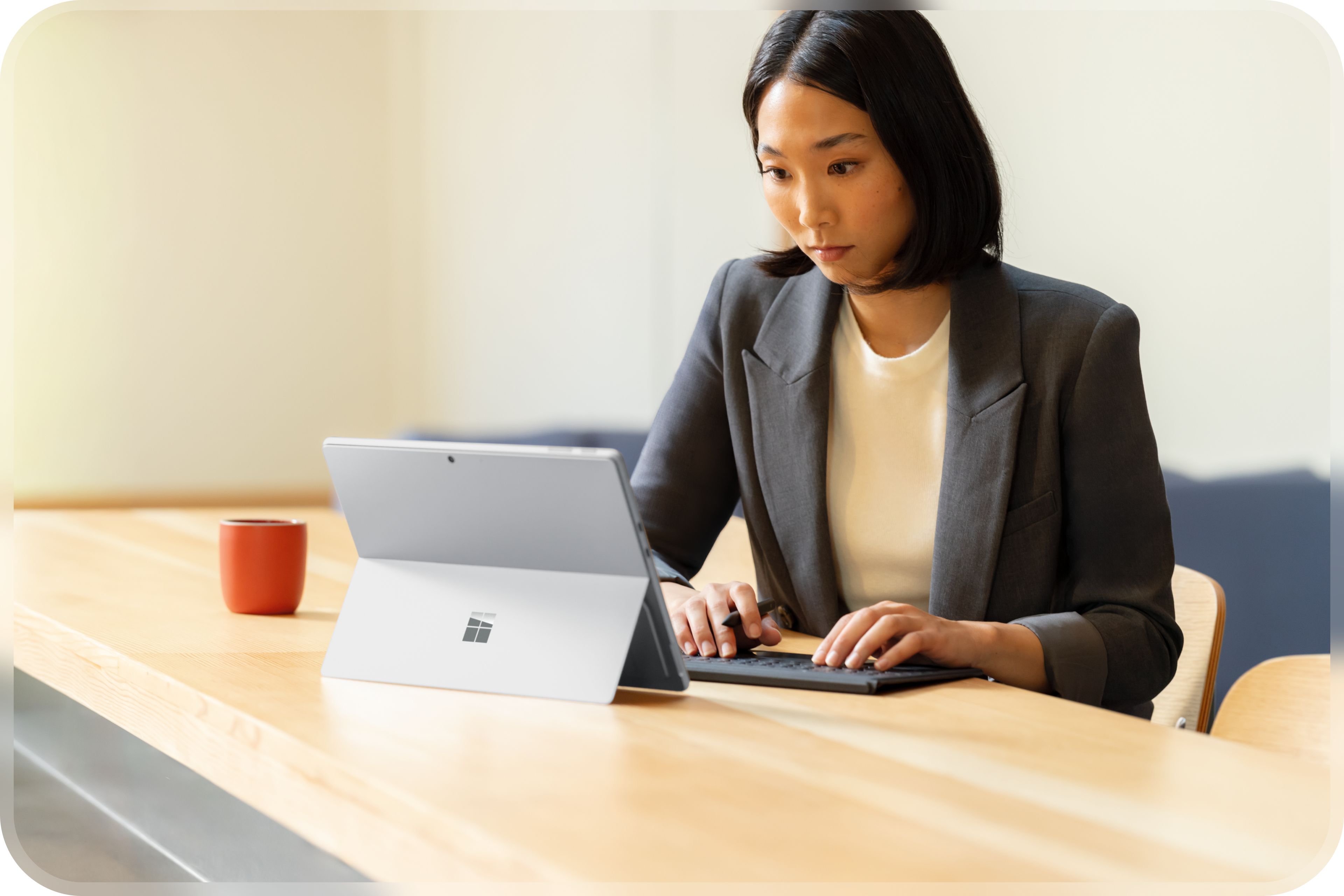 Un employé de bureau assis à une grande table de réunion en bois avec un ordinateur portable Windows ouvert avec clavier détaché et une tasse à café rouge