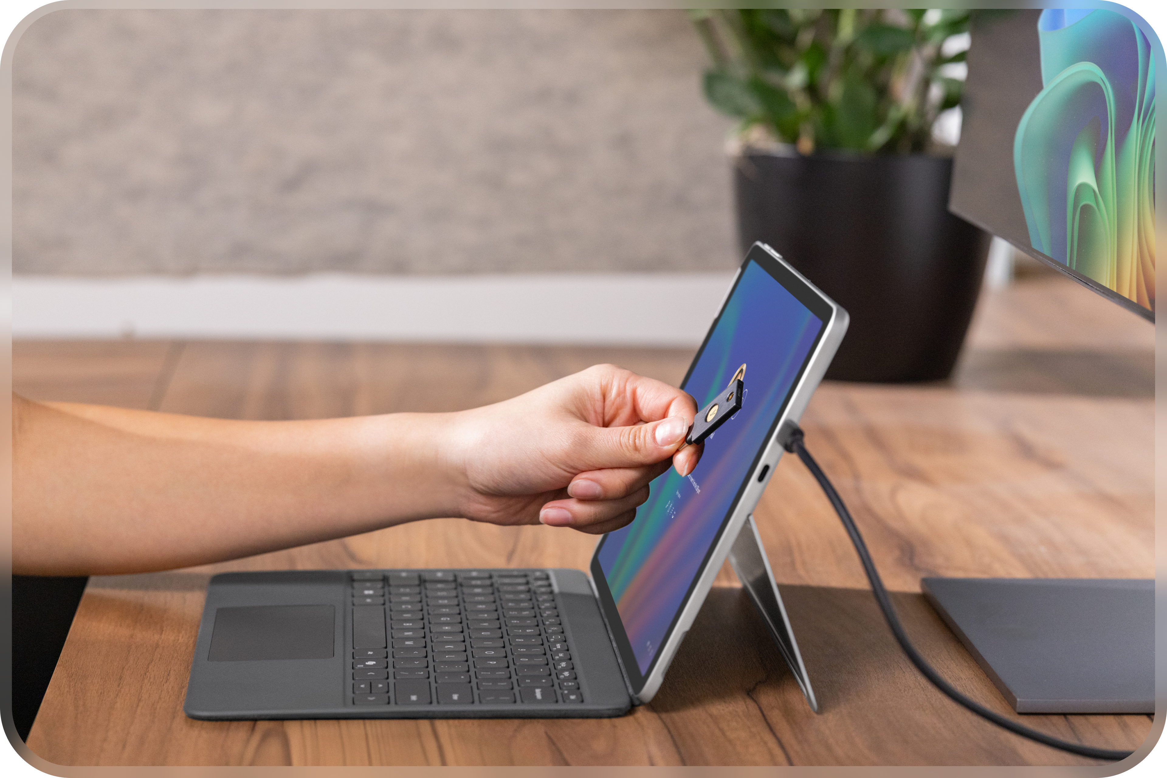 Un ordinateur portable Windows ouvert avec un écran externe posé sur un bureau affichant l'image de la fleur arc-en-ciel et une personne tenant une carte à puce sécurisée pour l'authentification, y compris la récupération simplifiée avec Pluton, BitLocker et Windows Hello.