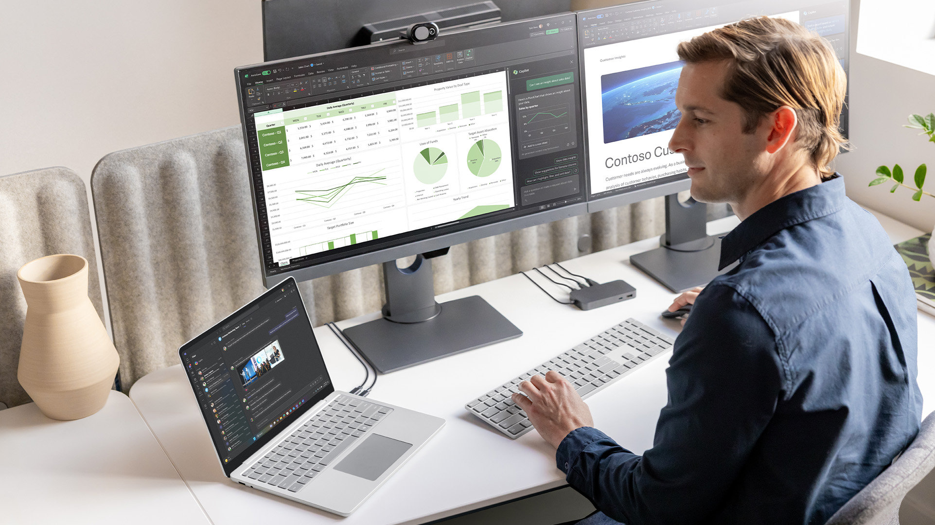 Office worker sitting at a workstation with an open Surface for Business device, a Surface USB4 Dock, and two external monitors each displaying several apps, including Teams, a data report, and a business webpage.