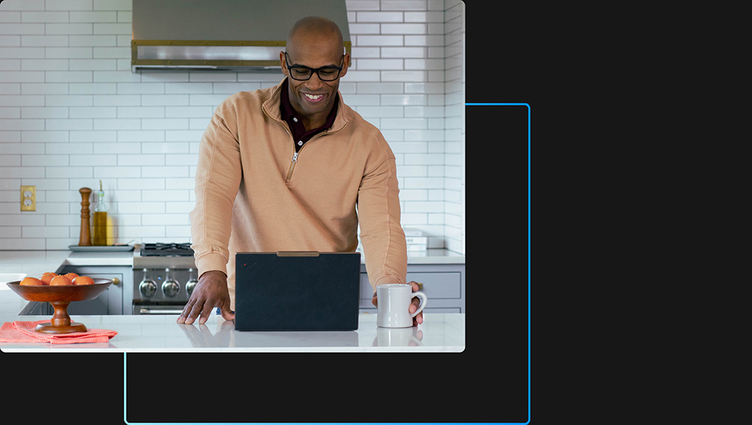 Een persoon in een keuken die op zijn of haar laptop werkt terwijl hij of zij lacht en een mok vasthoudt