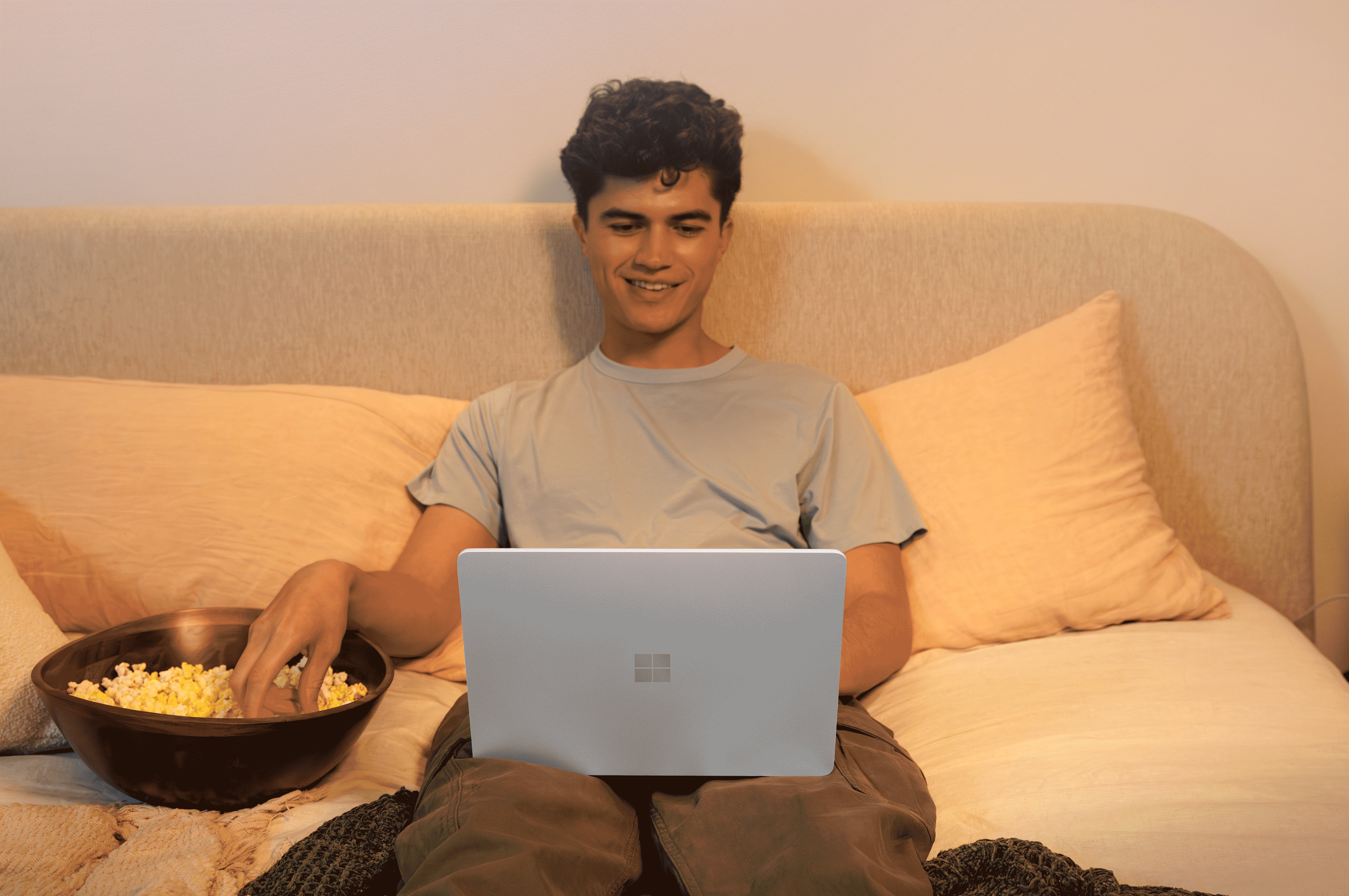 A person sitting on a couch with a bowl of popcorn, watching or working on a Surface laptop