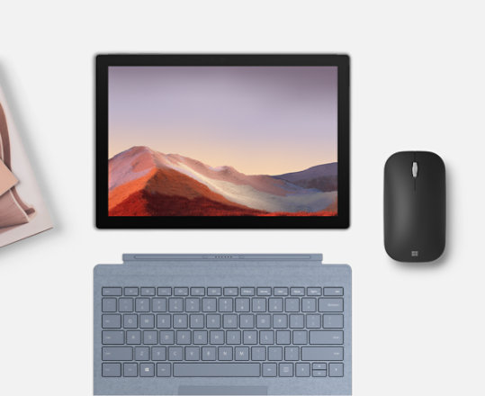 Microsoft Modern Mobile Mouse with a Surface device, keyboard, house plant, and several notebooks.