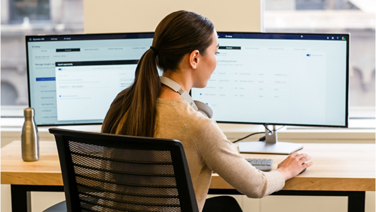 En person på ett kontor jobbar på sin bärbara dator med två bildskärmar och en mus