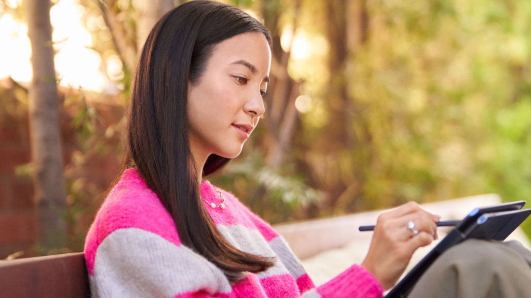 Une femme assise sur un banc de parc utilisant un stylo numérique sur son PC