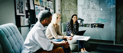 Three people are sitting and having a discussion in an office setting.