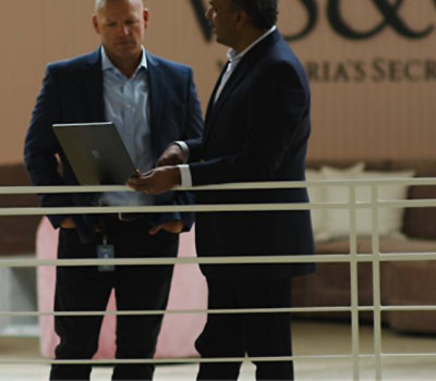 Two professionals in business attire standing and discussing over a laptop in an office setting.