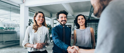 קבוצה של אנשים בלבוש עסקי עומדים בנוף משרדי, כשגבר אחד לוחץ ידיים לאדם