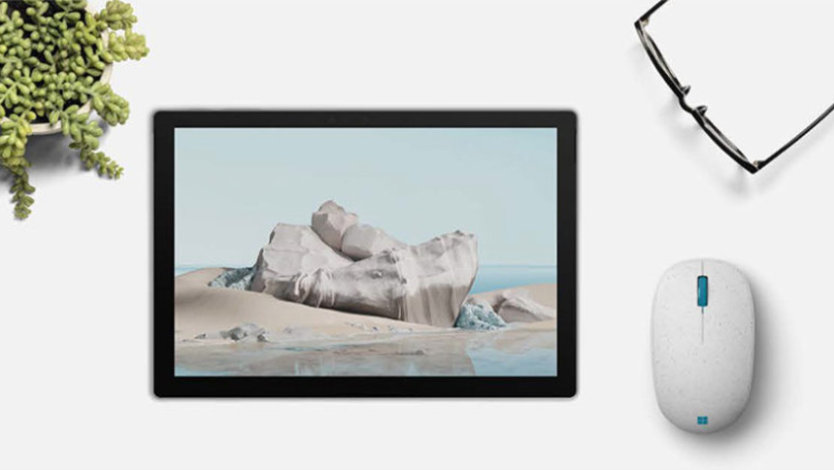 A tablet with an ocean screen, next to Microsoft Ocean Plastic Mouse and a pair of reading glasses