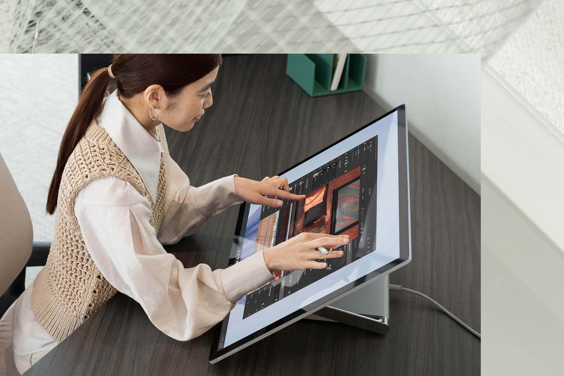 A person uses two hands to complete tasks while touching a Surface Studio 2+ in the office. 