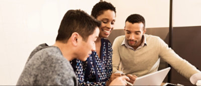 3 人がテーブルに座り、一緒にノート PC の画面を見ながら、集中して取り組んでいるように見えます。