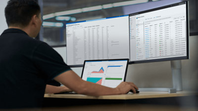 一个人在办公桌上用一台笔记本电脑和两台台式机屏幕工作。