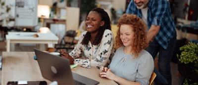 Due persone sedute in un ambiente interno, entrambe sorridono e sembrano ridere. Sullo sfondo un arredamento sfocato 