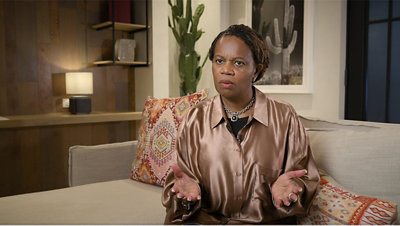 A lady with a necklace sitting on a sofa.