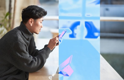 Mies harmaassa paidassa käyttämässä puhelintaan ja istumassa pöydän ääressä.