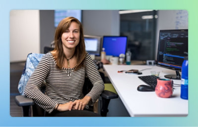 A woman sitting at a desk with a computer and a mug on it.