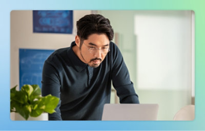 A man with glasses and a mustache looking at a laptop.