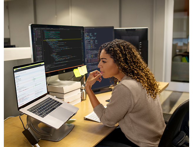 Žena, která sedí u stolu v kanceláři a dívá se na monitor počítače