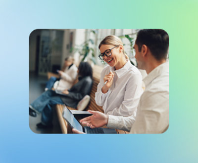 Two people are seated on a bench. The woman on the left is smiling and wearing glasses