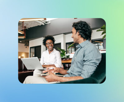 Two people sitting on a couch in a modern office setting, one holding a laptop and the other a tablet