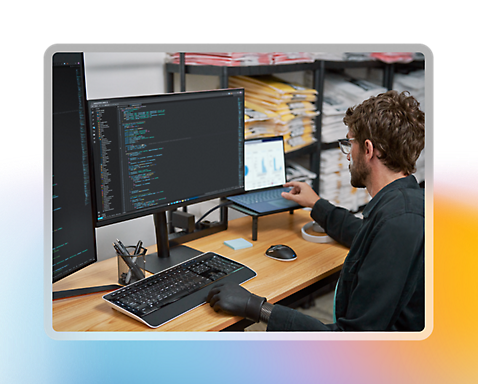 En person med briller og en kunstig hånd arbejder på en bærbar computer og flere skærme