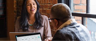 Two individuals in a meeting with one person looking at a laptop screen.